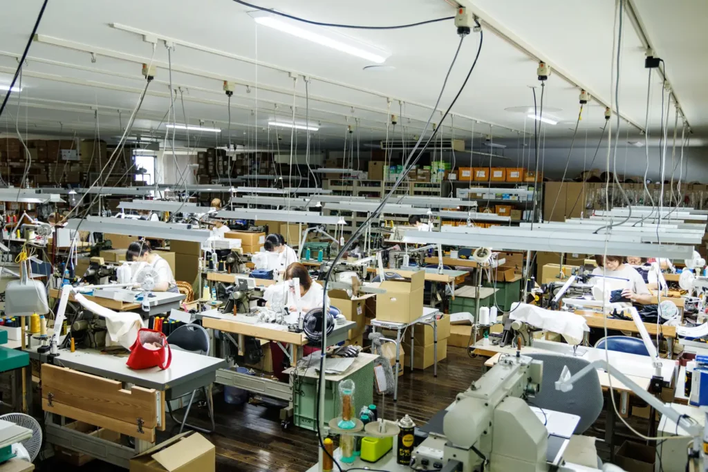 多数のミシンが並ぶ手袋製造工場の全景。熟練のスタッフがそれぞれのブースで縫製作業を行う様子